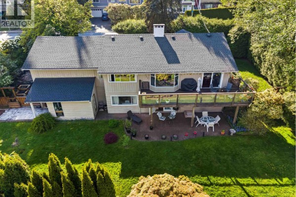 Rear view of a two-story home with a large deck, glass railings, and a grassy backyard. - 998 Fairway Drive, North Vancouver