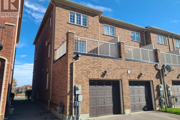 Side exterior view of brick townhouse with garage doors and upper-level balcony. - 9982 Mccowan Road, Markham