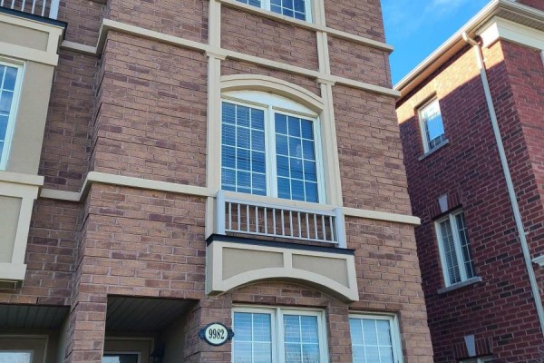 Close-up of brick facade with arched window, decorative trim, and balcony railing. - 9982 Mccowan Road, Markham