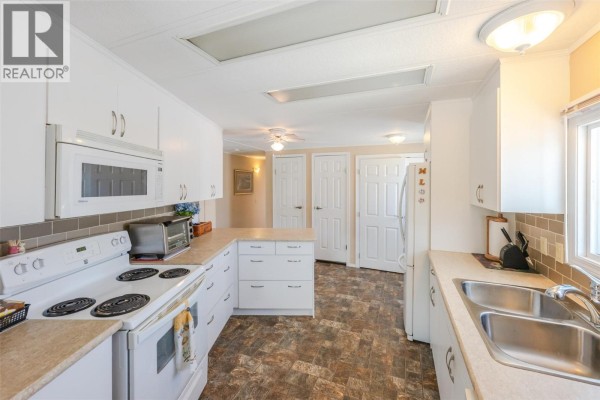 White kitchen with a double sink, stove, microwave, and cabinets. - 999 Burnaby Avenue Unit# 66, Penticton