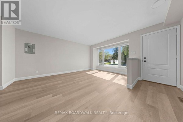 Living room with light wood laminate flooring, a large bay window, and a white door. - 999 Meadowlands Drive, Ottawa