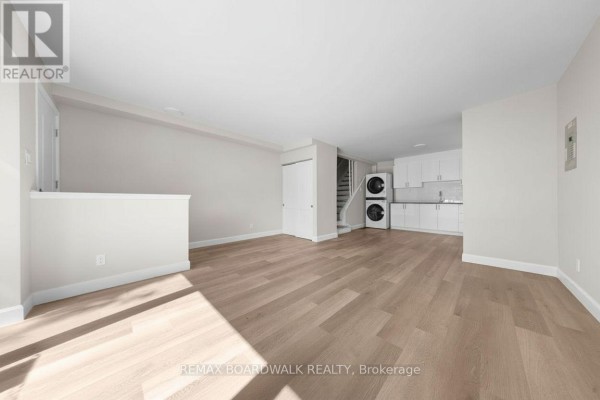 Living area with light wood laminate flooring, a white closet, and a small kitchen with stacked washer/dryer. - 999 Meadowlands Drive, Ottawa