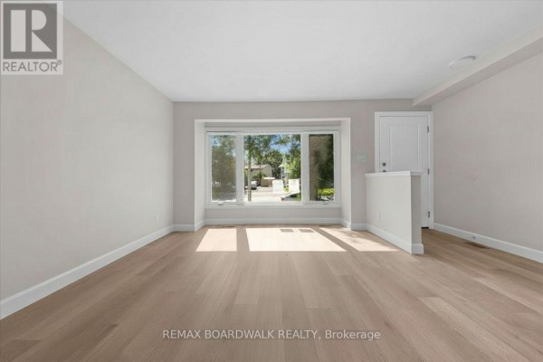 Living room with light wood laminate flooring, a white door, and a bay window facing the street. - 999 Meadowlands Drive, Ottawa