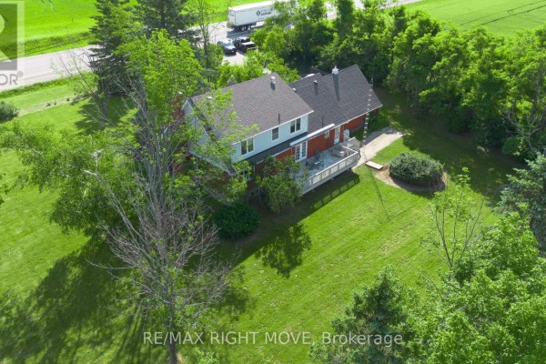Aerial view of the rear of a house with a wooden deck and surrounding trees. - 9992 Hwy 12 Highway, Oro Medonte