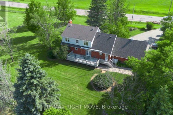 Aerial view of a red brick house with a white deck, visible from above and behind. - 9992 Hwy 12 Highway, Oro Medonte