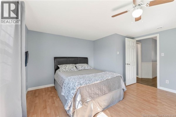 Bedroom with a queen-size bed, light blue walls, wood-paneled doors, and wood laminate flooring. - 99a Glebe Road, Chamcook