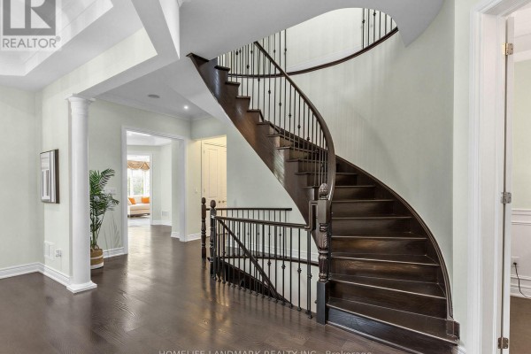 Hallway with dark hardwood floors and a dark wood curved staircase with ornate railings. - 9a Anglin Drive, Richmond Hill