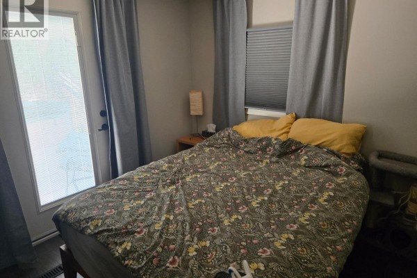 Bedroom with a queen-size bed, yellow pillows, and a glass door leading outside. - 9a Riva Ridge Estates, Penticton