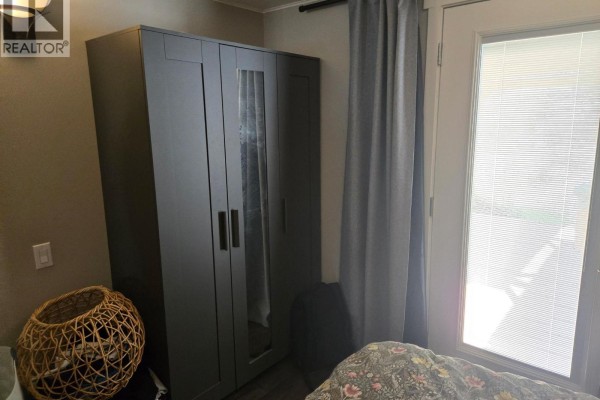 Bedroom with a grey wardrobe featuring mirrored doors and a glass door leading outside. - 9a Riva Ridge Estates, Penticton