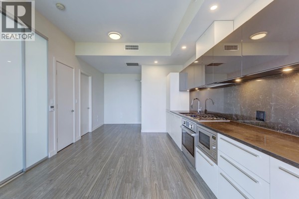 Kitchen with white cabinets, dark countertop, stainless steel appliances, and hallway entrance. - 9xx 6383 Mckay Avenue, Burnaby
