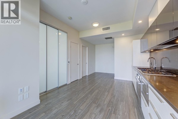 Kitchen with white cabinets, stainless steel appliances, dark backsplash, and entrance doors. - 9xx 6383 Mckay Avenue, Burnaby