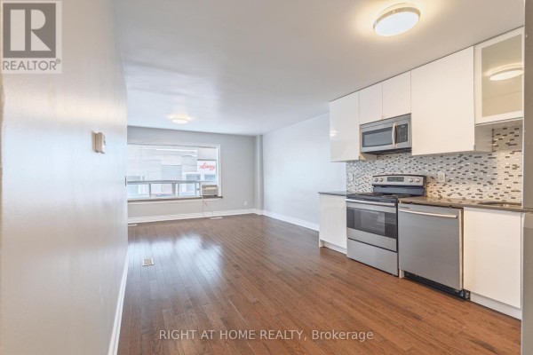 Open concept living area and kitchen with dark hardwood floors and white cabinets. - A - 1132 The Queensway Avenue, Toronto