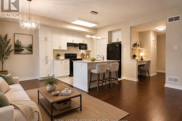 Kitchen with white cabinetry, granite countertops, island with bar stools, and adjacent living area. - A - 20 Tadley Private, Ottawa