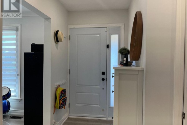 Entranceway with a white door, light wood floor, and a white shoe cabinet with a round mirror above. - A - 38 Wishing Well Drive, Toronto