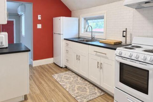 Kitchen area with white cabinets, black countertops, white stove, and red accent wall. - A - 9 Francis Street W, Kawartha Lakes