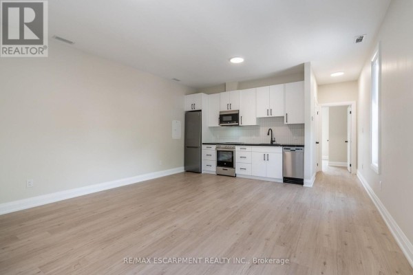 A wide view of a studio apartment showing the kitchen and living area with light wood floors. - A - 9 Munn Street, Hamilton