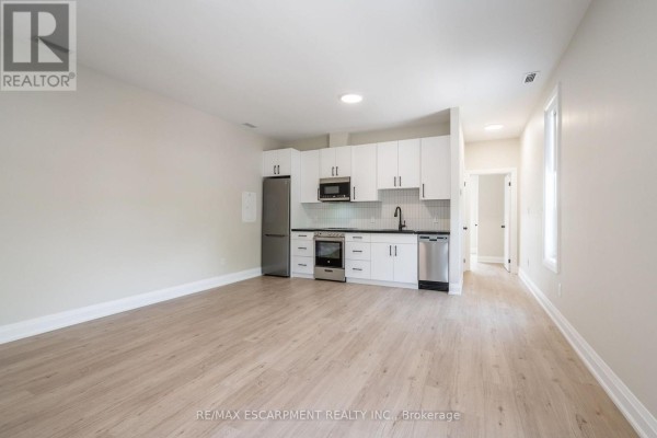A studio apartment layout with a kitchen on the left and a hallway leading to a doorway on the right. - A - 9 Munn Street, Hamilton
