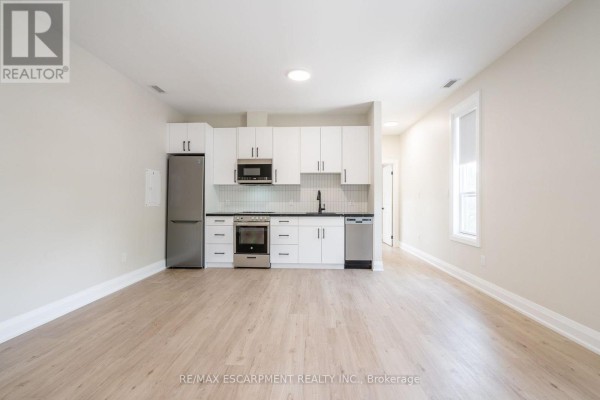 Close-up of a compact kitchen with white cabinets, stainless steel appliances, and black hardware. - A - 9 Munn Street, Hamilton