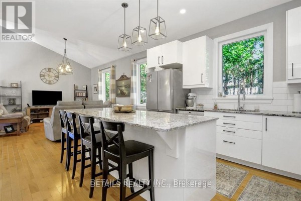 Open concept kitchen with white cabinets, granite island with black stools, and stainless steel appliances. - A - Upper Unit - 2565a Page Road, Ottawa