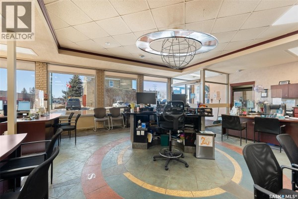Office space with desks, chairs, computers, and large windows showing street views. - A 100 Fairford Street W, Moose Jaw