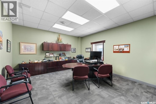 Private office with a large desk, chairs, cabinetry, and framed pictures on light green walls. - A 100 Fairford Street W, Moose Jaw