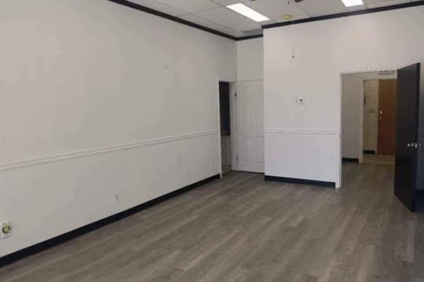 Interior view of an empty commercial space with white paneled walls, grey wood-look flooring, and black trim. - A 387 Parkview Road, Yorkton