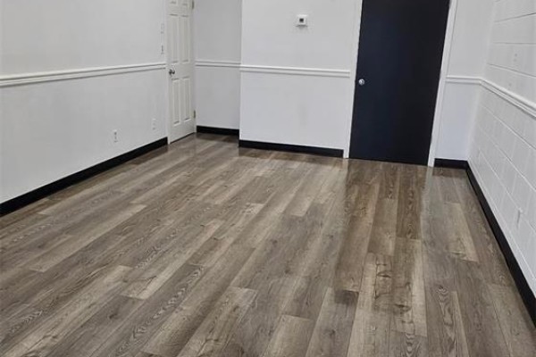 Corner of an empty commercial space with white walls, grey wood-look flooring, and black baseboards. - A 387 Parkview Road, Yorkton