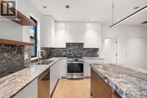 Spacious kitchen featuring white cabinets, a large marble island, and a stainless steel stove. - A 9650 Third St, Sidney