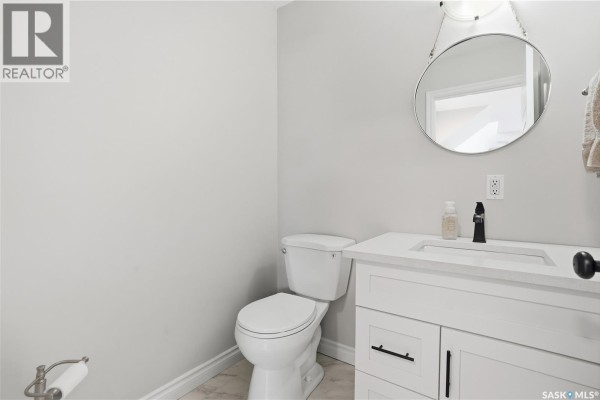 Powder room with a white vanity, sink, black faucet, toilet, and round mirror. - A-b 141 Queen Street, Elbow