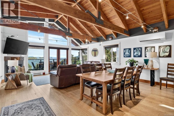 Living and dining room with a fireplace, large windows, wooden dining table, and seating. - A-g 118 Rainbow Rd, Salt Spring