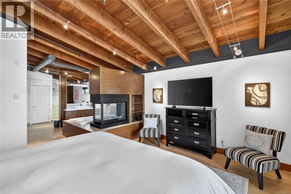 Bedroom with a fireplace, television, dresser, and striped chairs, with an open bathroom area. - A-g 118 Rainbow Rd, Salt Spring