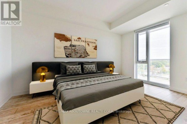 Bedroom with king-size bed, grey headboard, and window overlooking the city. - A0815 - 125 Bronte Road, Oakville