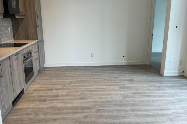 Empty living space with light laminate flooring, looking towards the kitchen and an open doorway. - A1405 - 8119 Birchmount Road N, Markham