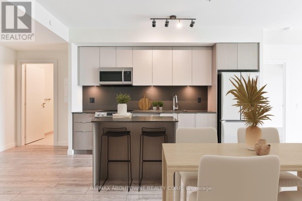Modern kitchen with light wood cabinetry, stainless steel appliances, and a breakfast bar with two stools. - A303 - 125 Bronte Road, Oakville