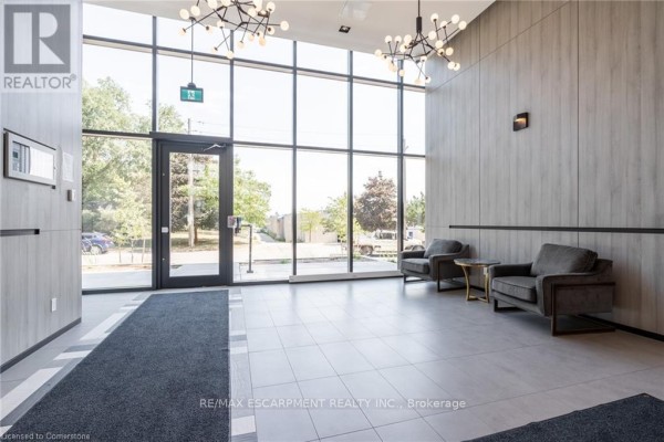 Apartment building lobby with gray tiled floor, two armchairs, and large windows. - A305 - 1117 Cooke Boulevard, Burlington