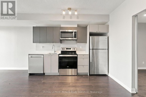 Modern kitchen with grey and beige cabinets, stainless steel appliances, and dark wood flooring. - A312 - 3210 Dakota Common, Burlington
