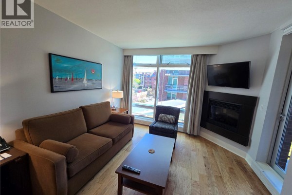 Living room with sofa, coffee table, armchair, fireplace, and a painting on the wall. - A316 810 Humboldt St, Victoria