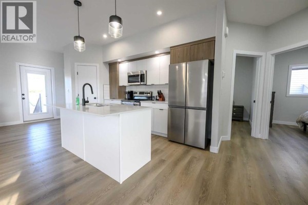 Open concept kitchen with white island, stainless steel appliances and light wood floors. - B, 10478 131 Avenue, Grande Prairie