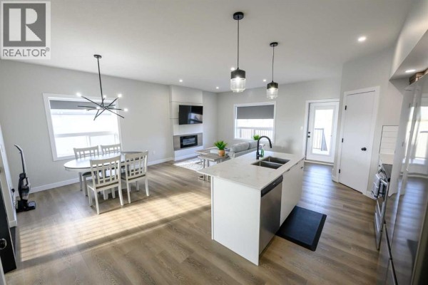 Living and dining area with white table, fireplace and island with sink. - B, 10478 131 Avenue, Grande Prairie