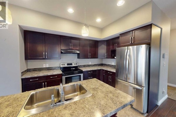 Dark wood kitchen cabinets, stainless steel refrigerator, and granite countertop with sink. - B, 13022 91a Street, Grande Prairie