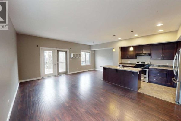 Open concept living area with dark wood floors, kitchen island, and patio doors. - B, 13022 91a Street, Grande Prairie