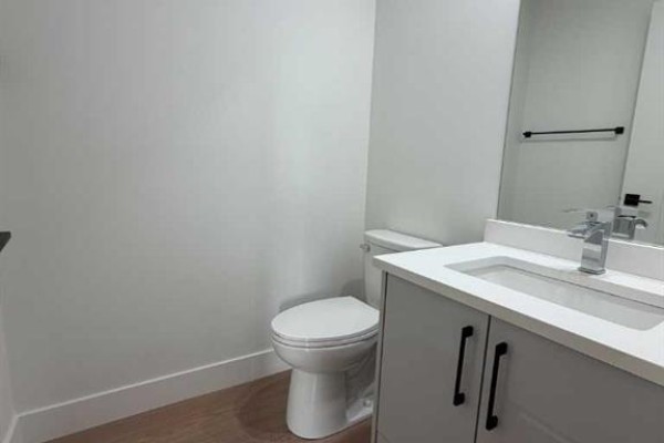 Powder room with a white toilet, a vanity with a white countertop, and a large mirror. - C, 9403 103 Avenue, Grande Prairie