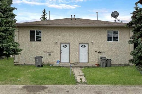 Rear exterior of the duplex with beige stucco siding, two white doors, and green grass. - B, 9406 100 Avenue, Grande Prairie