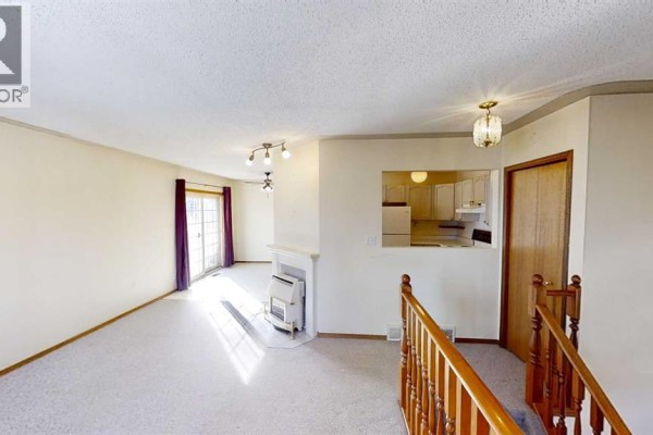 Living room with light beige carpet, white walls, a white fireplace, and a doorway to the kitchen. - B, 9406 100 Avenue, Grande Prairie