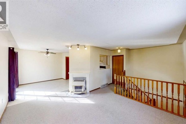 Living room with beige carpet, white walls, a fireplace, and a view of the kitchen and hallway. - B, 9406 100 Avenue, Grande Prairie