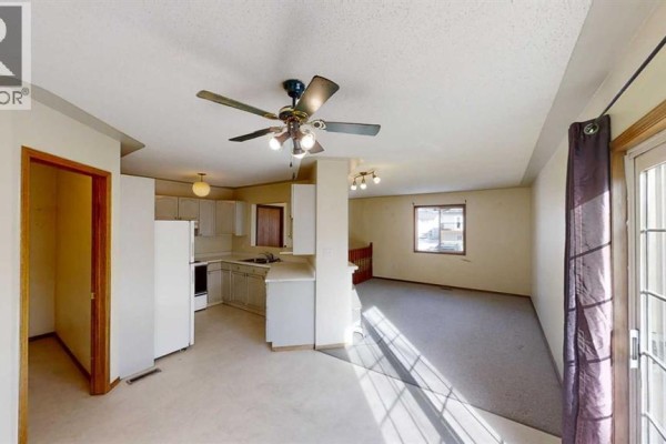Kitchen and living area with white cabinets, beige carpet, and a sliding glass door. - B, 9406 100 Avenue, Grande Prairie