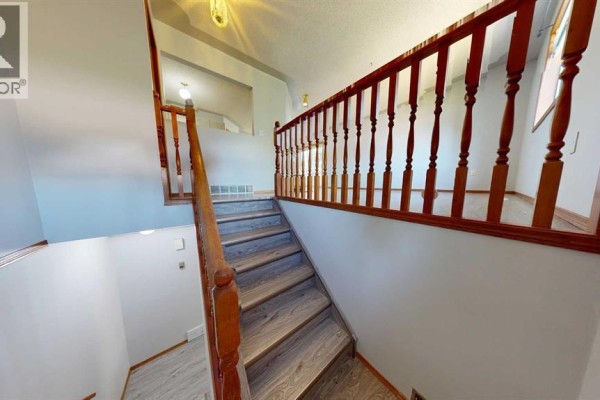 Interior view of a staircase with wood railings and light grey laminate flooring. - B, 9408 100 Avenue, Grande Prairie