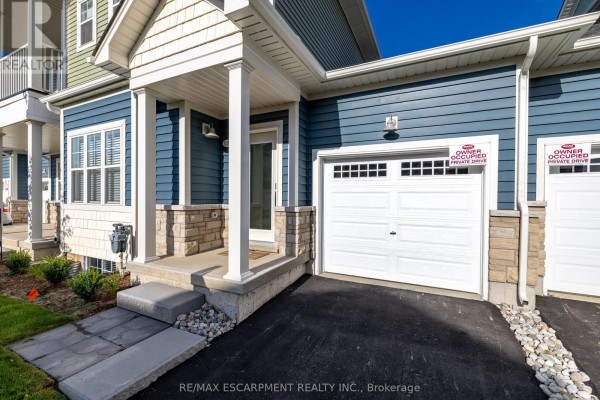 Close-up of townhouse entrance with blue siding, stone details, and a white garage door. - B - 10 Shores Lane, Fort Erie