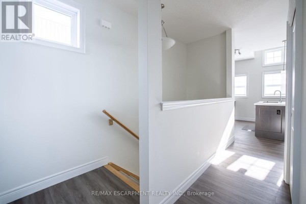 Interior hallway view with white walls, wood-look flooring, and stairs leading down. - B - 10 Shores Lane, Fort Erie