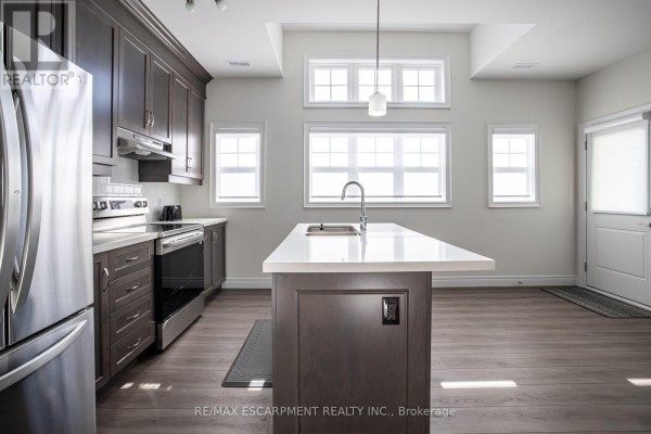 Kitchen with dark wood cabinets, stainless steel appliances, and an island with a white countertop. - B - 10 Shores Lane, Fort Erie